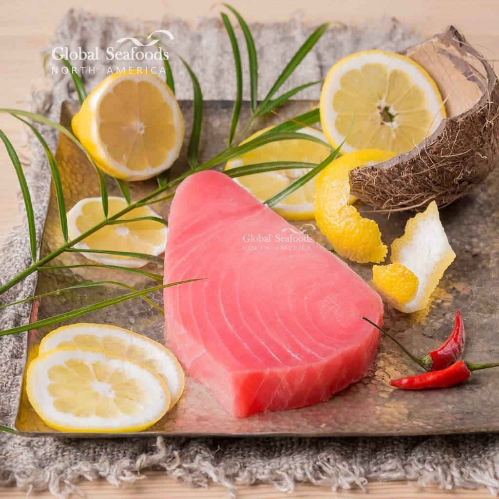 Raw tuna steak on a wooden board with lemons, coconut, and chili peppers, branded 'Global Seafoods'.